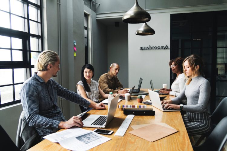 A group of employees around a desk with laptops having a meeting in a modern office room.