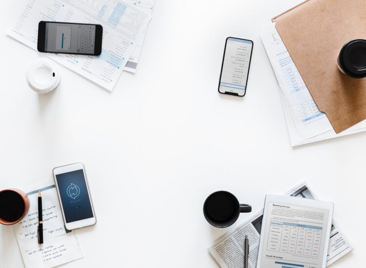 an image of a table with phones, paper, folders and cups of coffee on it.