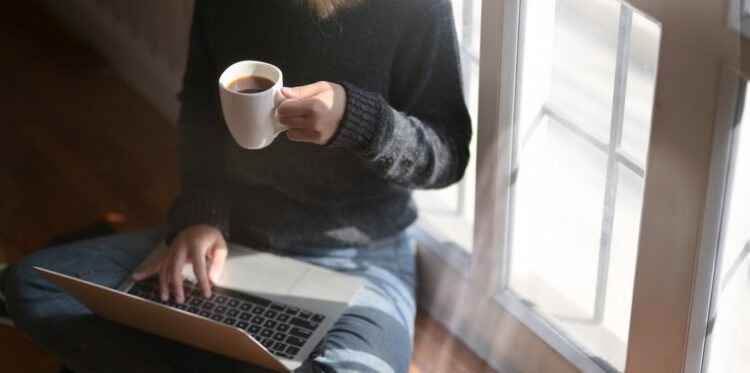 A woman holding a cup of coffee while using her laptop.
