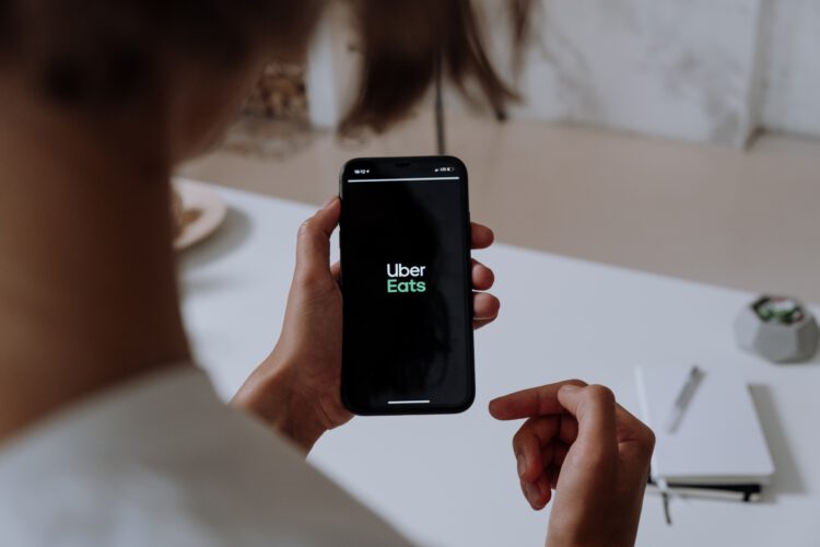 An image of a woman looking at her phone displaying the Uber Eats logo.