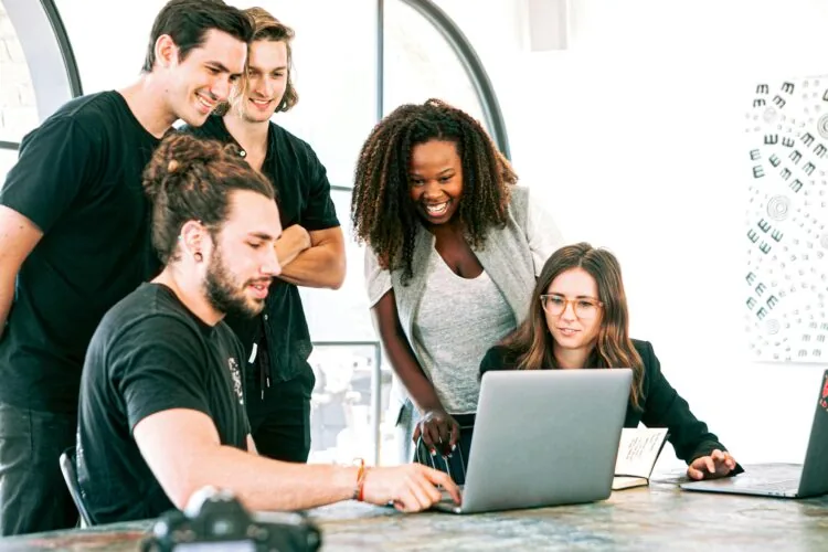 An image of a team gathered around a laptop to discuss a project.